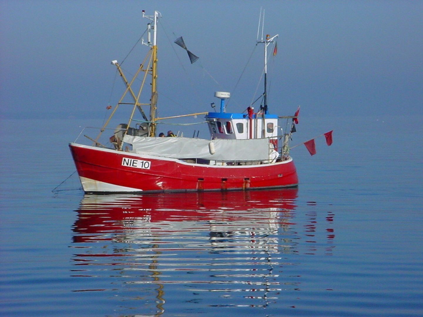 En rød og hvid fiskebåd med identifikationsnummer NIE 10 på stille vand.