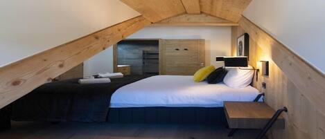A bedroom with a sloped ceiling, a bed, a bedside table, and a wardrobe.