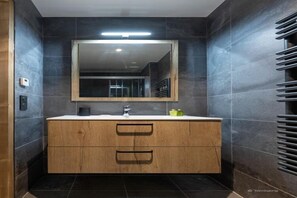 A modern bathroom with dark tiled walls, a wooden vanity with a mirror, and a towel rack. - Chalet in Chantemerle with Sunny Ski Slopes (Saint Chaffrey)