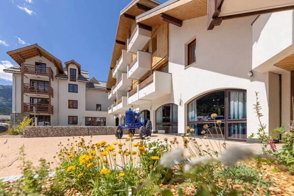 A multi-story hotel with balconies, a covered outdoor area, and a blue tractor parked in front. - Chalet in Chantemerle with Sunny Ski Slopes (Saint Chaffrey)