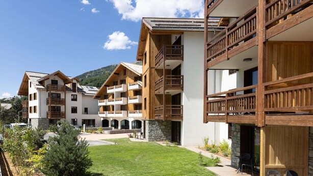 A modern hotel with multiple balconies, a well-maintained lawn, and stone accents. - Apartment in Chantemerle with Family Ski Fun (Saint Chaffrey)