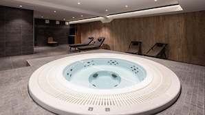 Un moderno espacio interior de spa con una bañera de hidromasaje central, sillones reclinables y una zona de estar.
