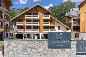 A multi-story lodge with a stone wall entrance, wooden balconies, and a sign reading "CRISTAL LODGE TERRESENS." - Apartment in Chantemerle near Serre-Chevalier (Saint Chaffrey)