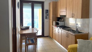 A compact kitchen with wooden cabinets, a dining table with chairs, a microwave, a gas stove, and a sink. - Angy Apartment (San Tommaso Tre Archi)