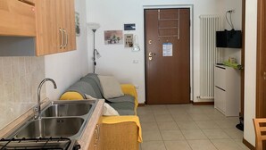 A compact kitchen with a sink, stove, and a small dining area with a couch. - Angy Apartment (San Tommaso Tre Archi)