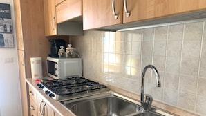 A kitchen with wooden cabinets, a gas stove, a microwave, and a stainless steel sink. - Angy Apartment (San Tommaso Tre Archi)