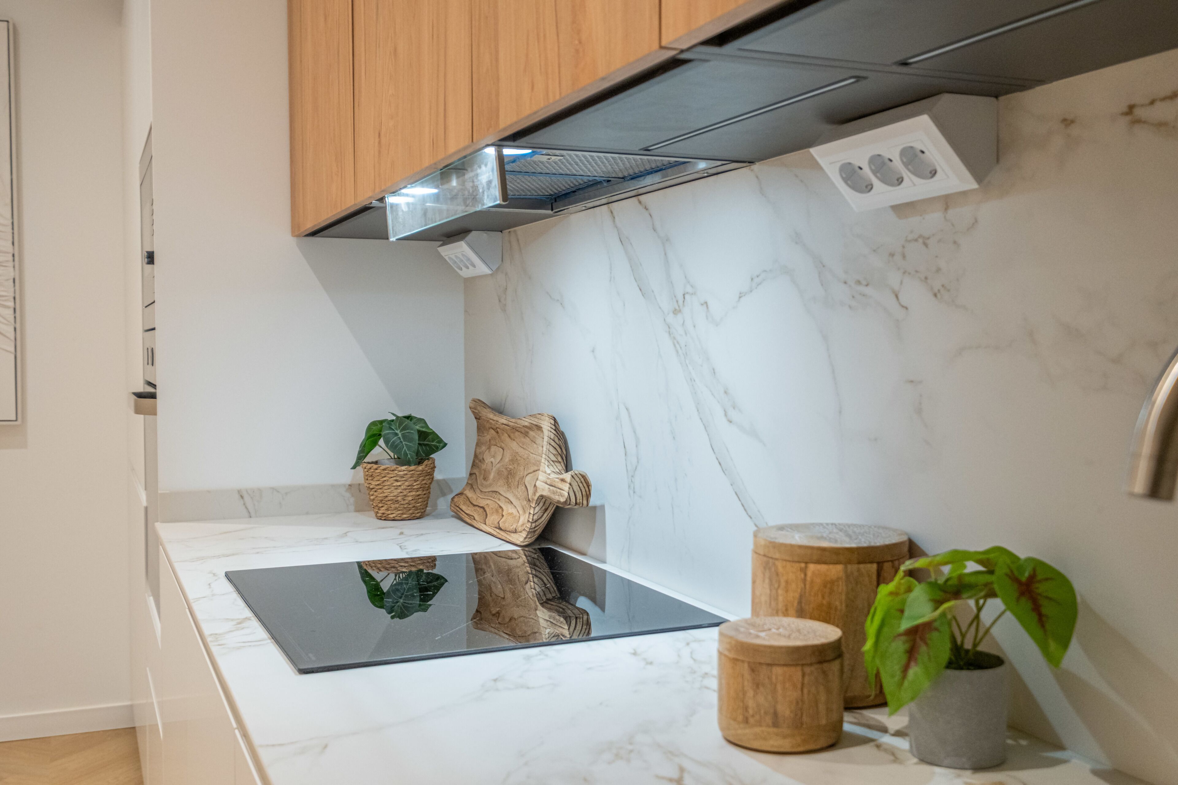 A modern kitchen with a marble countertop, wooden cabinets, a built-in stove, and decorative items.