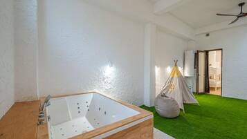 Un baño moderno con tocador de madera, una bañera grande y una estructura tipo tienda en el suelo.