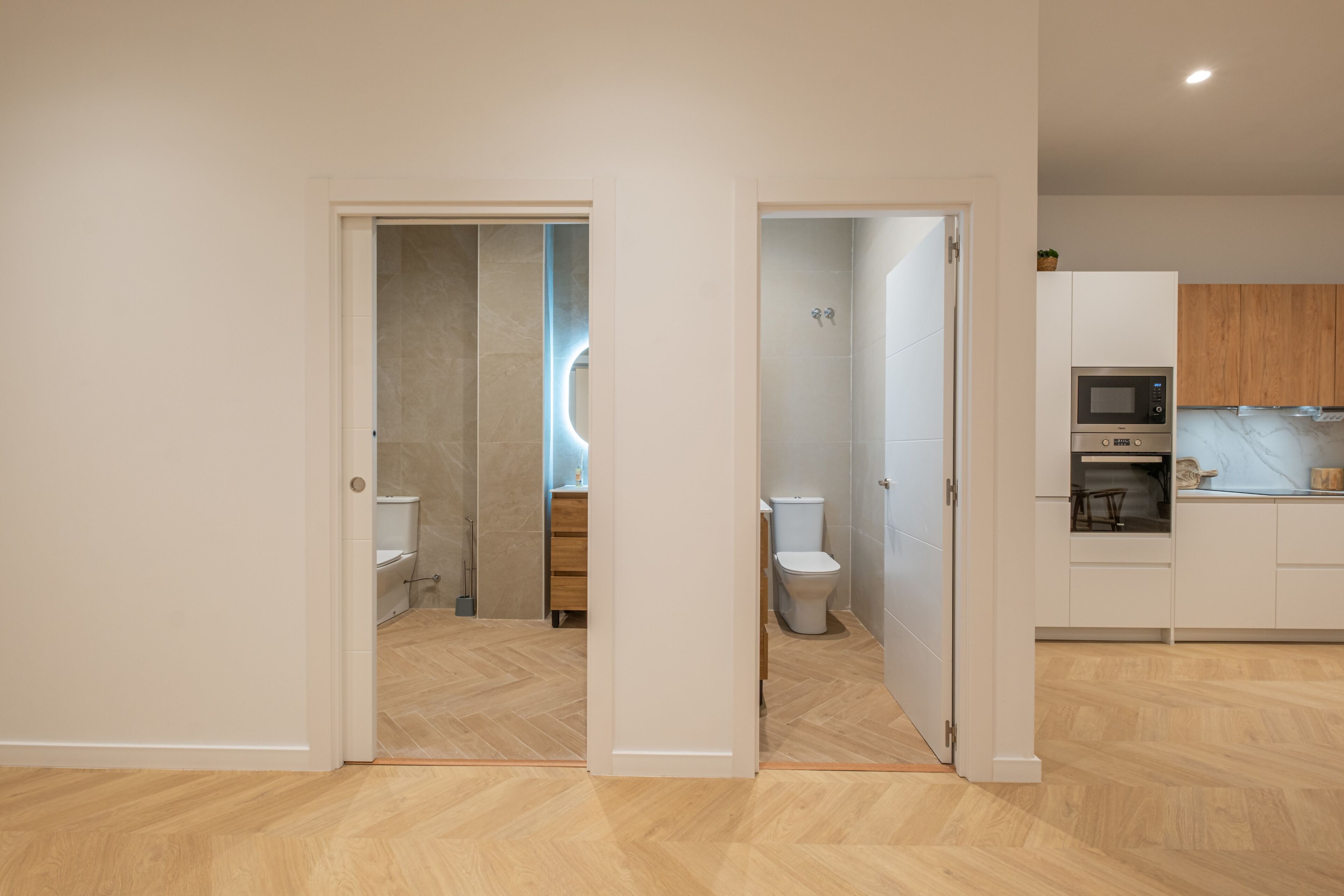 Un apartamento moderno con piso de madera, cocina con armarios blancos y baño con ducha e inodoro.