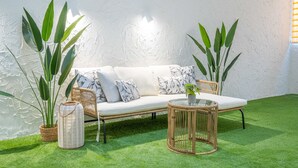A white sofa with patterned cushions, a wicker coffee table, and large green plants. - Flats - Poeta Serrano (Valencia)