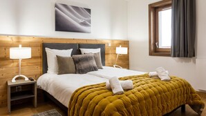 Ein ordentlich bezogenes Bett mit einer senfgelben Steudecke, zwei Nachttischlampen und einem Holzkopfende.