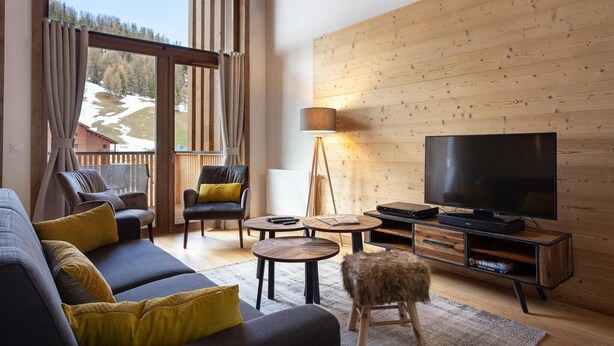 Un salon moderne comprenant un canapé, deux fauteuils, une table basse, un téléviseur et un mur en bois.
