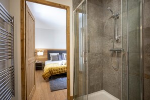 Une chambre d’hôtel avec une douche, un lit recouvert d’une couverture jaune et une porte en bois.