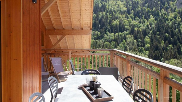 A wooden deck with a table and chairs, overlooking a forested valley. - Apartment in Serre Chevalier Ski Resort (VAUJANY)