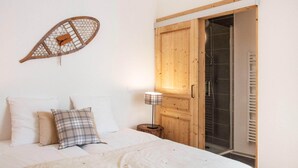 A bedroom with a bed, pillows, a wall-mounted decorative item, a wooden door, and a small table with a lamp. - Apartment in Serre Chevalier Ski Resort (VAUJANY)