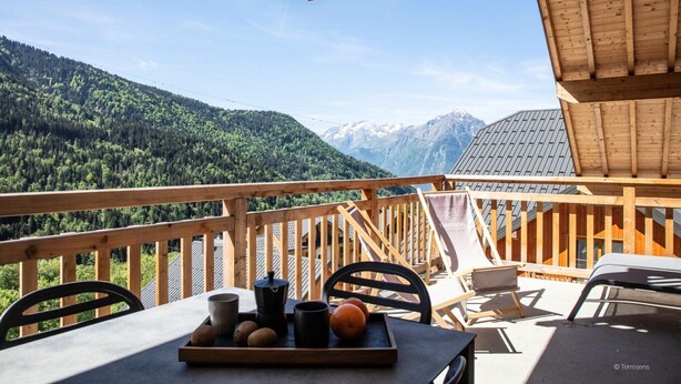 Terraza de madera con una mesa dispuesta para el desayuno, con vistas a un paisaje montañoso.