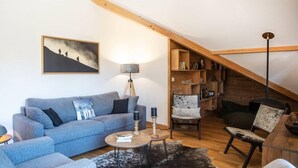 Una sala de estar acogedora con un sofá gris, una mesita redonda y una estantería bajo un techo inclinado.