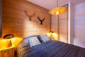 A bedroom with a wooden wall, a bed with patterned pillows, and two bedside lamps.