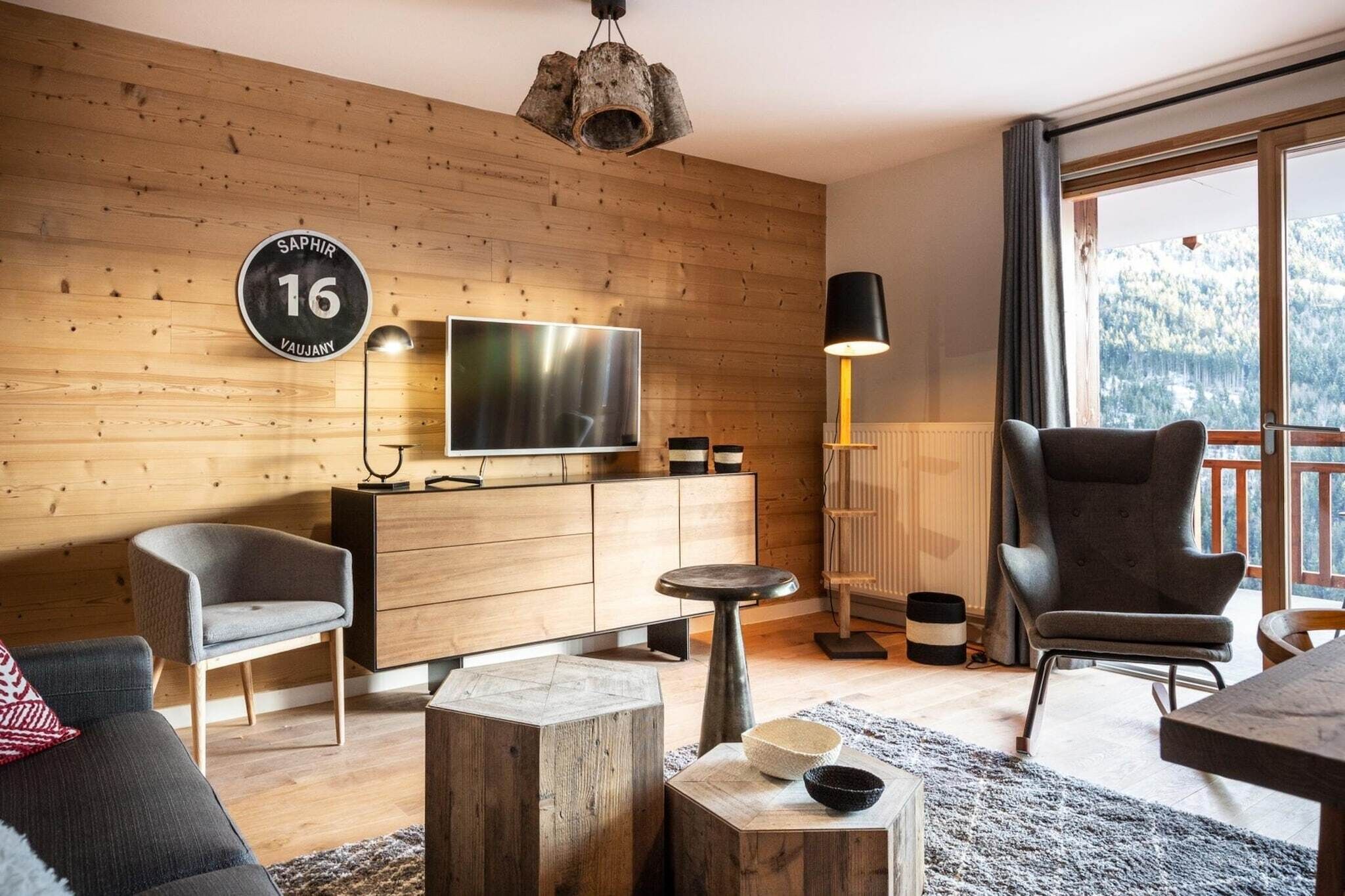Una sala de estar moderna con una pared de madera, un televisor de pantalla plana, un sofá, un sillón, una mesa de centro y un ventanal con vistas a la montaña.