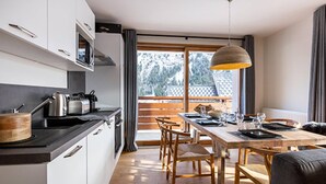 A modern kitchen with white cabinets, a wooden dining table, and a view of a balcony with a wooden railing.