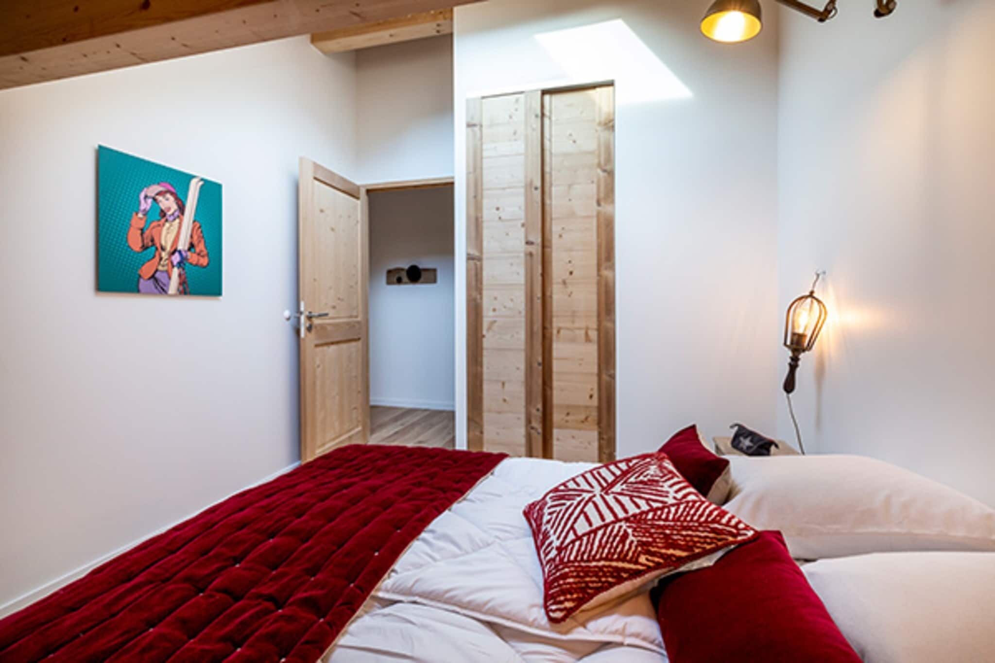 Une chambre à coucher avec un lit, une couverture rouge, un oreiller blanc, un autre oreiller rouge, une décoration murale, une armoire en bois et un luminaire.