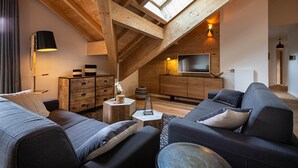 Un moderno salón tipo loft con techo alto, vigas de madera, un televisor grande y un rincón de estar acogedor.