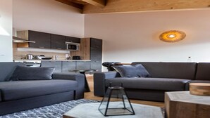 Una sala de estar moderna con dos sofás grises, techo de madera y una cocina al fondo.