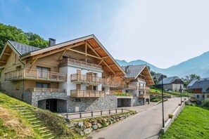 A modern chalet-style building with a stone facade, wooden balconies, and a stone entrance.