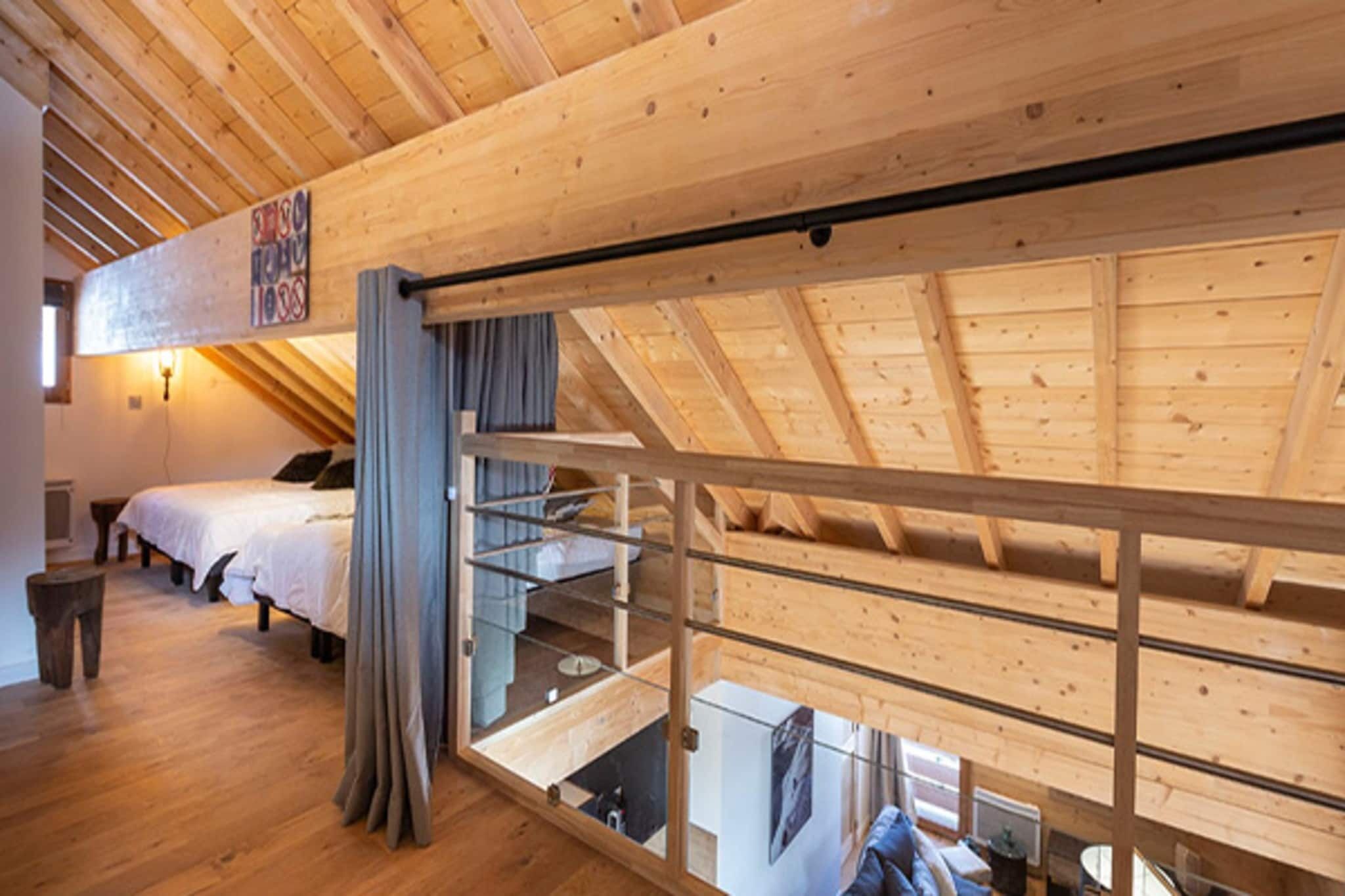 Un dormitorio con techo inclinado, vigas de madera, una cama, un escritorio y una ventana.