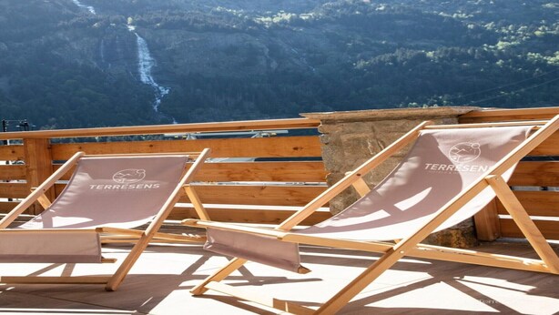 Dos sillones de madera con la marca 'Terresens', frente a un paisaje montañoso con una cascada.