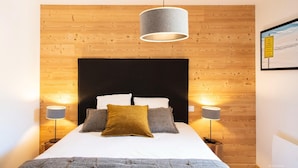 Un dormitorio con pared de madera, cabecero negro y dos lámparas de noche.