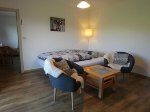 Un salon chaleureux avec un canapé, deux fauteuils, une table basse et un tableau accroché au mur.