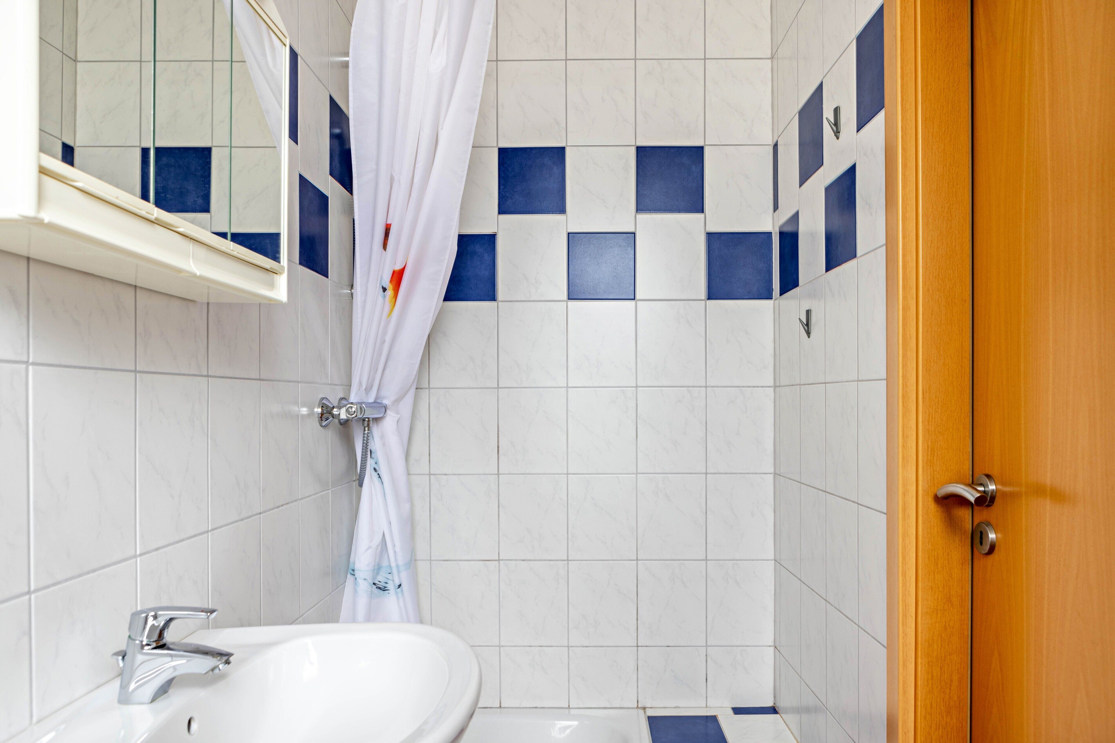 Un baño con un lavabo blanco, cortina de ducha y puerta de madera.