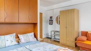 A bedroom with a bed, wooden wardrobe, and a small table with a mirror.