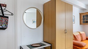 A room with a wooden wardrobe, a round mirror, a small table with a tray, and a bed with orange bedding.