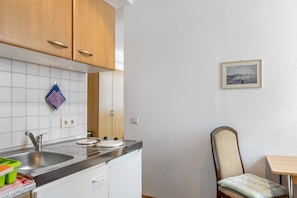 A kitchen with a sink, stove, and cabinets; a chair and table; and a framed picture on the wall.