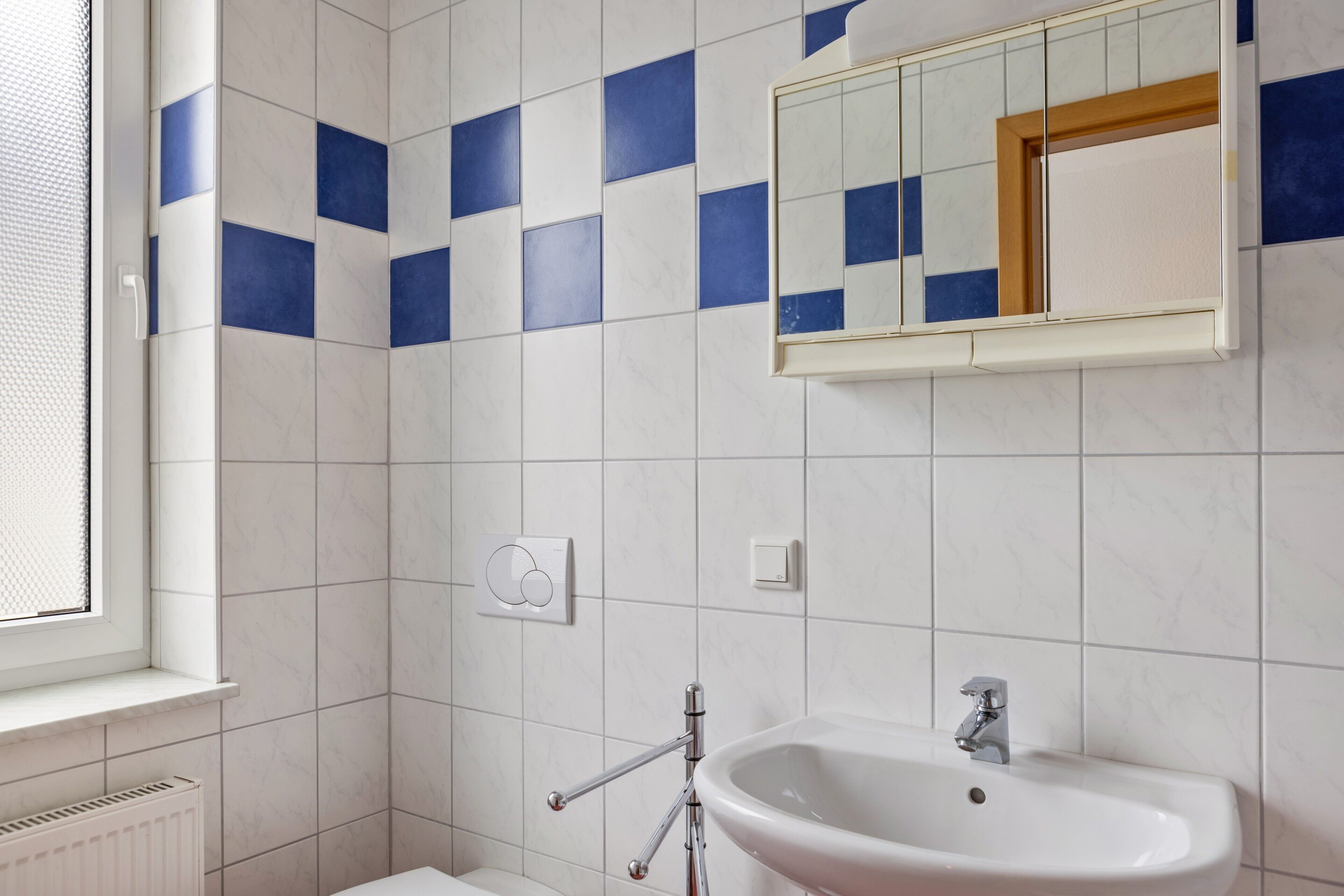A bathroom with a white sink, a mirror, and a window.