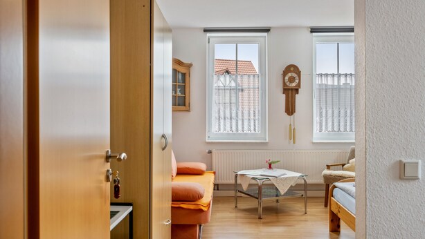 A room with a bed, a table, a chair, a radiator, and a window with a view of a building.
