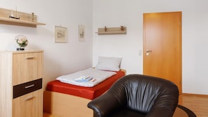 Ein Schlafzimmer mit einem Bett, einem Holzschrank, einem schwarzen Ledersessel und einer Holztür.
