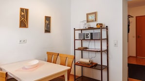 Ein Essbereich mit Tisch, Stühlen, einem Regal mit Küchengeräten und gerahmten Bildern an der Wand.