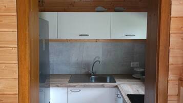 A compact kitchen with wooden walls, a stainless steel sink, white cabinets, and a sign above the door.