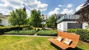 Un jardin avec un banc en bois, un sentier et un bâtiment doté d’une tour.