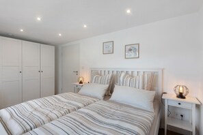 Un dormitorio con dos camas, paredes blancas y una mesita de noche con lámpara.
