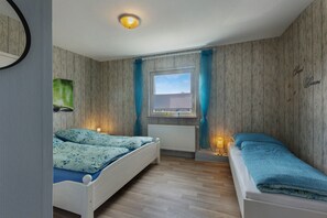 Un dormitorio con dos camas, una ventana con cortinas, un radiador y una lámpara fijada a la pared.