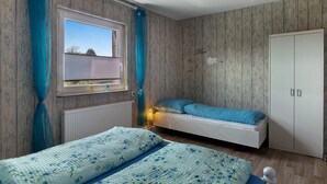 Un dormitorio con cama, armario, ventana con cortinas y radiador.