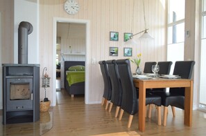 A cozy room with a wood-burning stove, a dining table with chairs, and a bed with a green blanket.