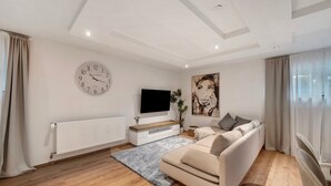Una sala de estar moderna con un sofá, un televisor de pantalla plana, un reloj y un cuadro grande en la pared.