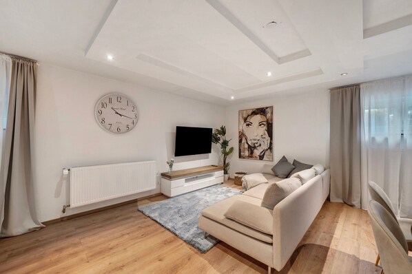 A modern living room with a sofa, a flat-screen TV, a clock, and a large painting on the wall.