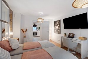 A modern bedroom with two beds, a desk, and a TV.