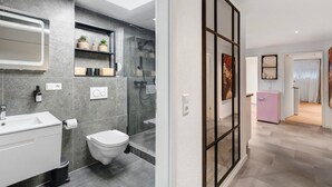Un baño moderno con ducha, inodoro y lavamanos; un pasillo con una puerta; y un refrigerador rosa pequeño.